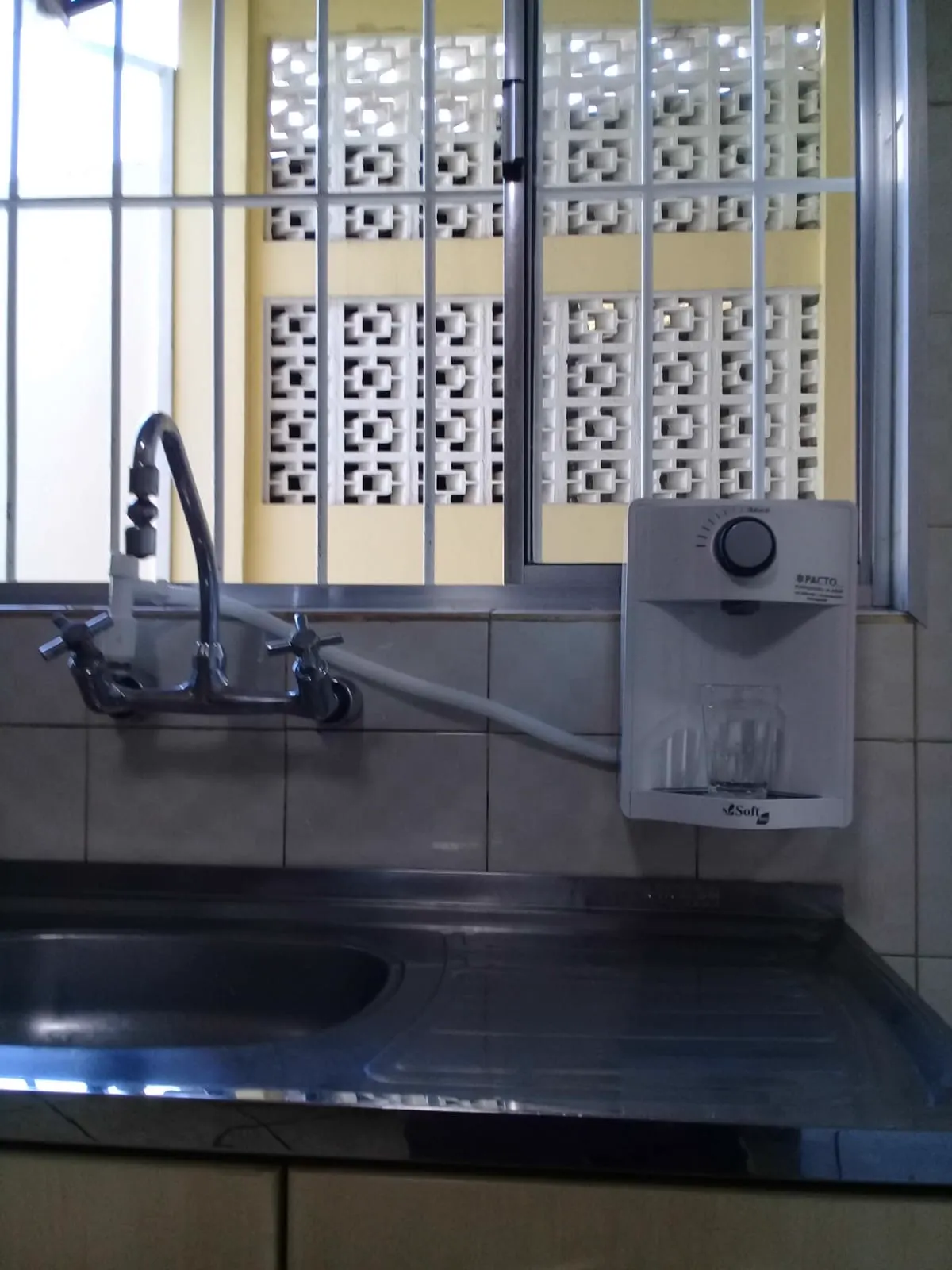 Purificador de água branco instalado em parede de cozinha acima de pia de inox