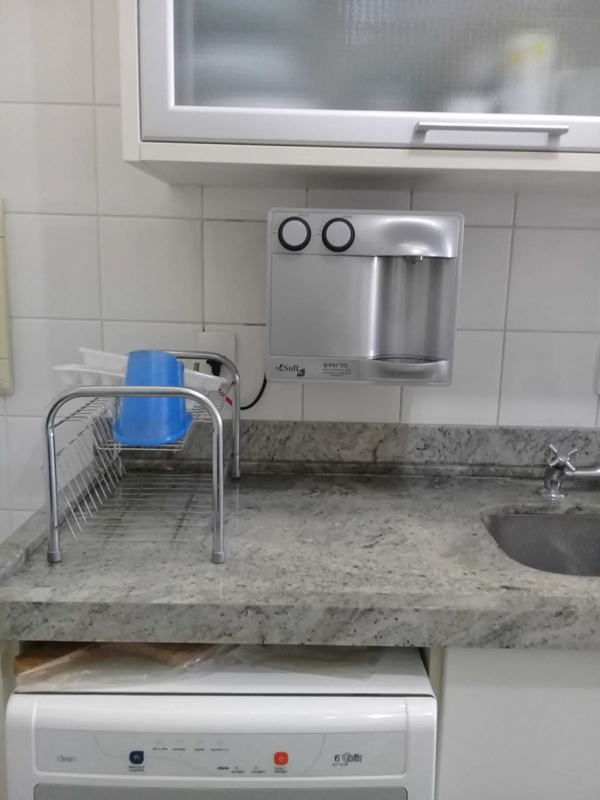 Purificador de água prata instalado em parede branca acima de bancada de granito claro