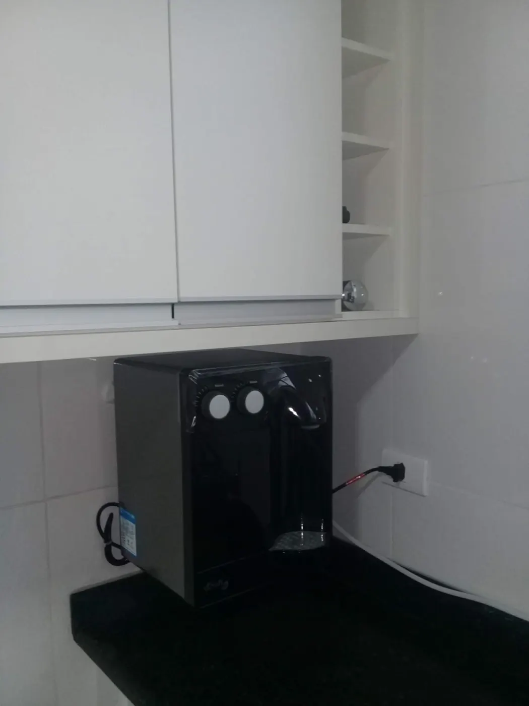 Purificador de água Soft preto instalado em bancada de granito preto sob armário planejado