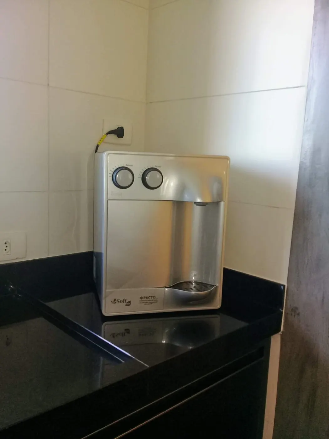 Purificador de água Soft prata apoiado em bancada de granito preto em cozinha residencial