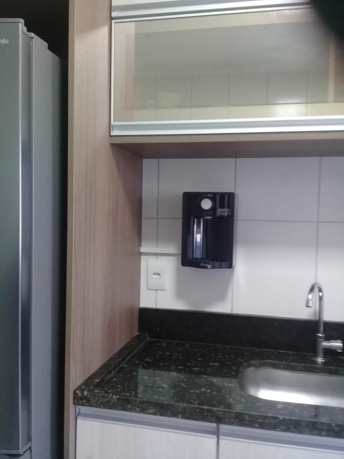 Purificador de água preto instalado na parede acima da pia de um apartamento