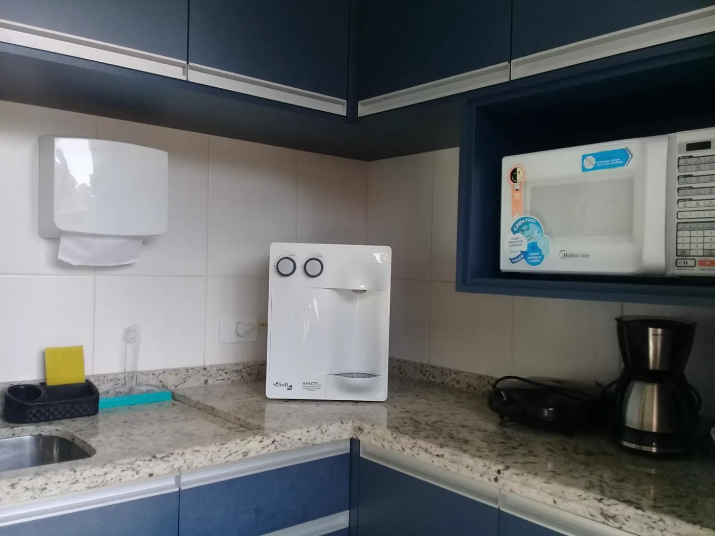 Purificador de água branco sobre bancada de granito claro em cozinha com armários azuis