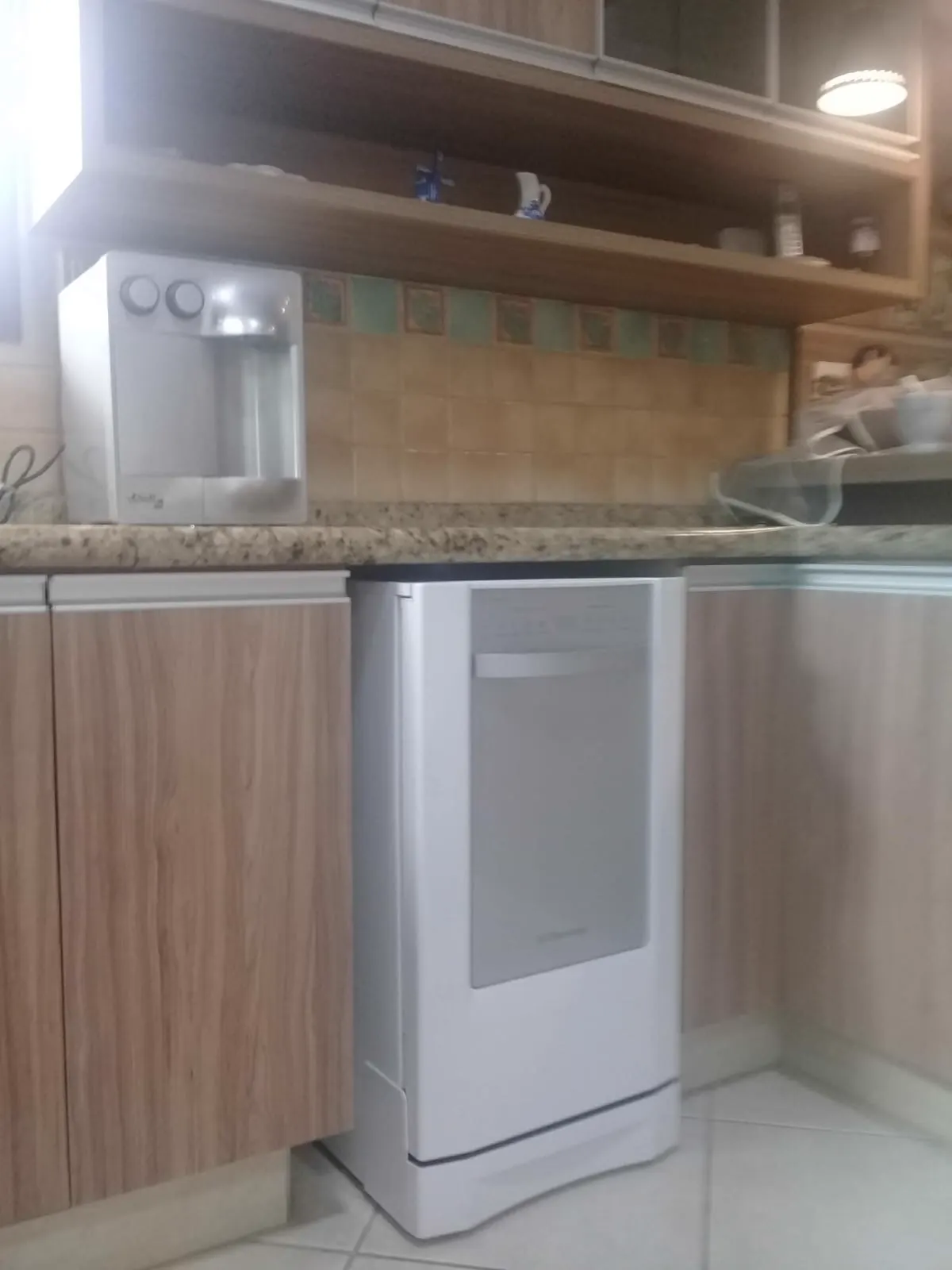 Purificador de água branco sobre bancada de granito claro em cozinha com prateleiras de madeira