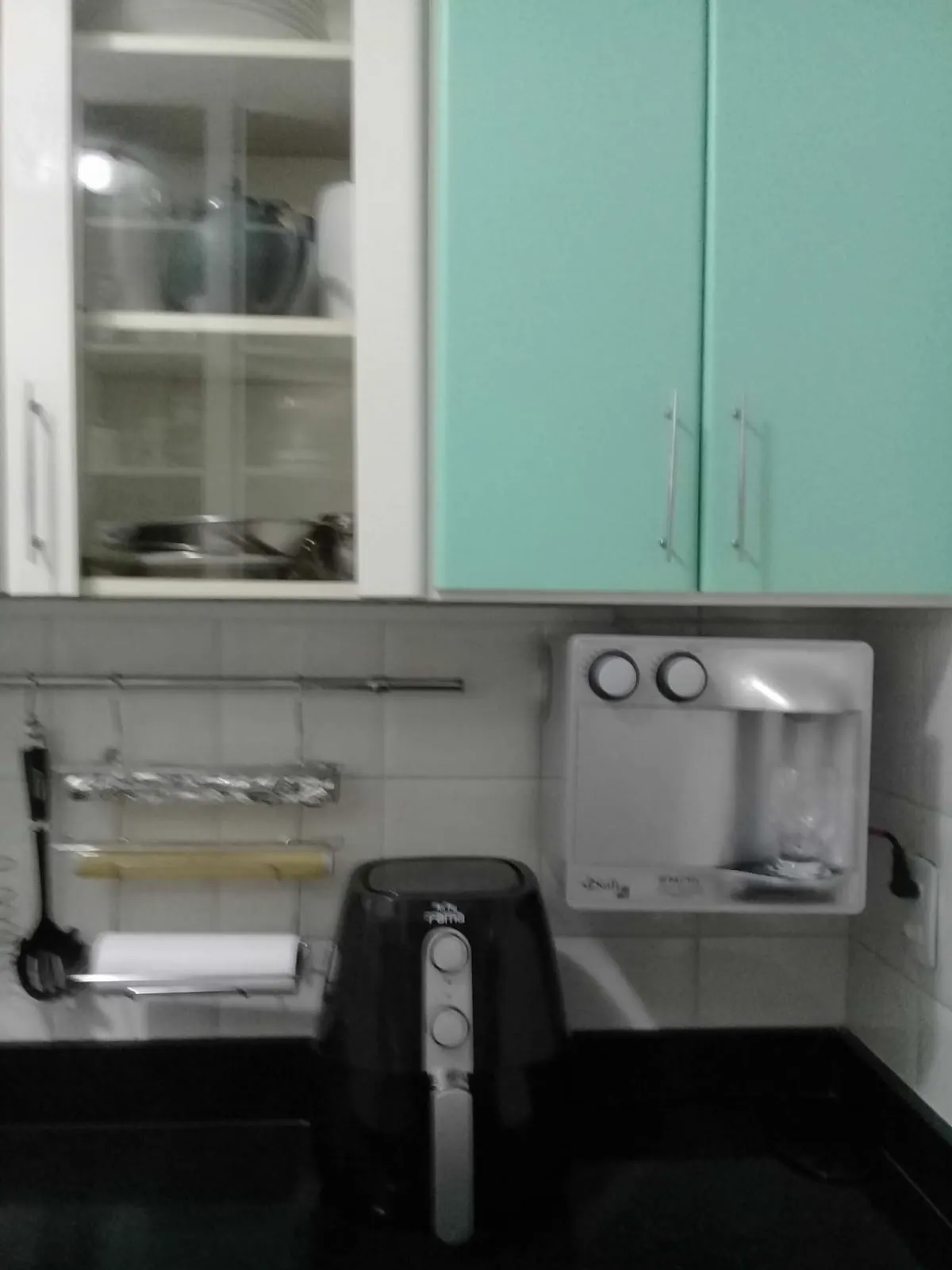 Purificador de água branco instalado em parede de cozinha com armários verdes