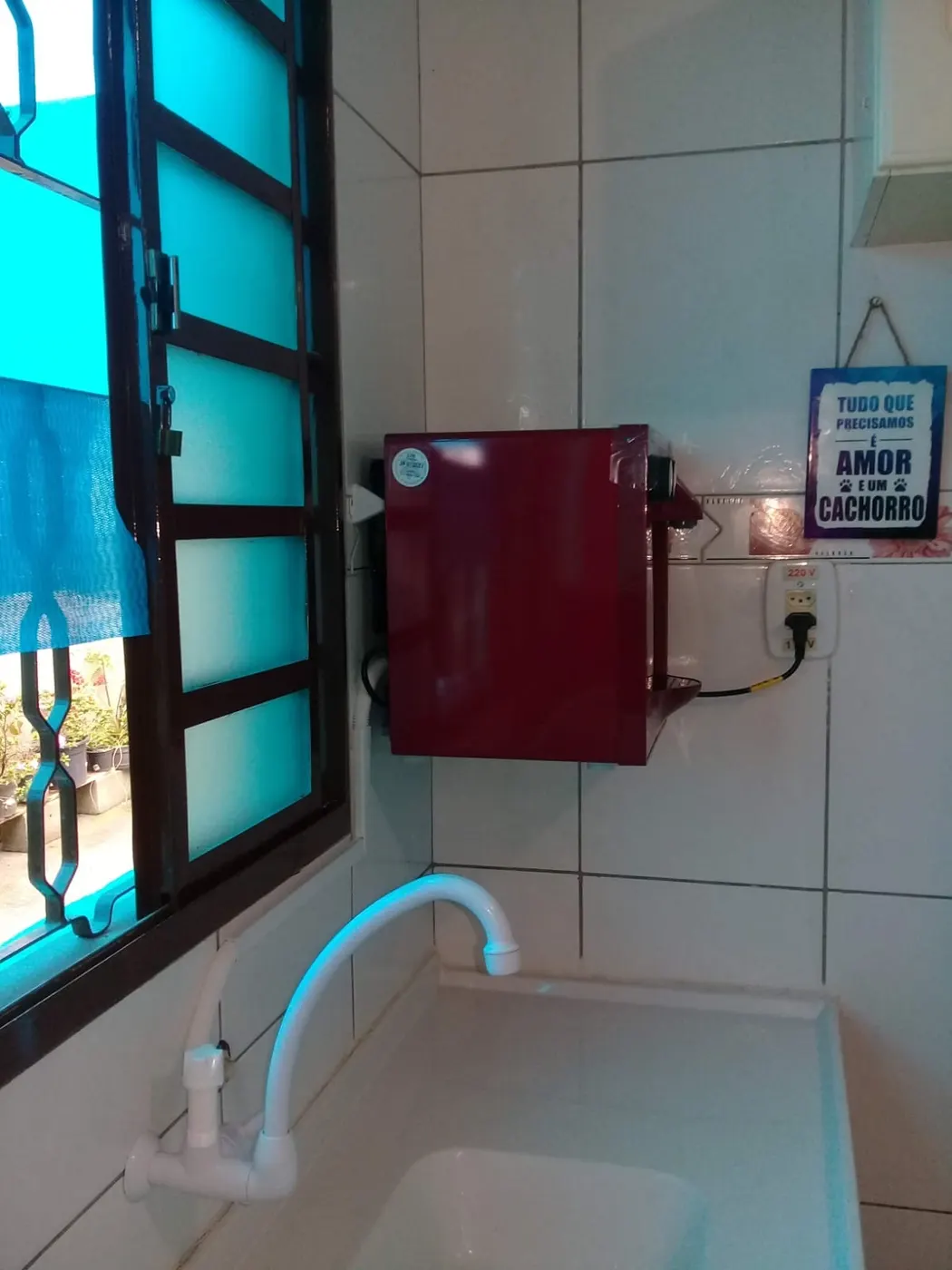 Purificador de água Soft vermelho instalado em parede de azulejo acima da pia