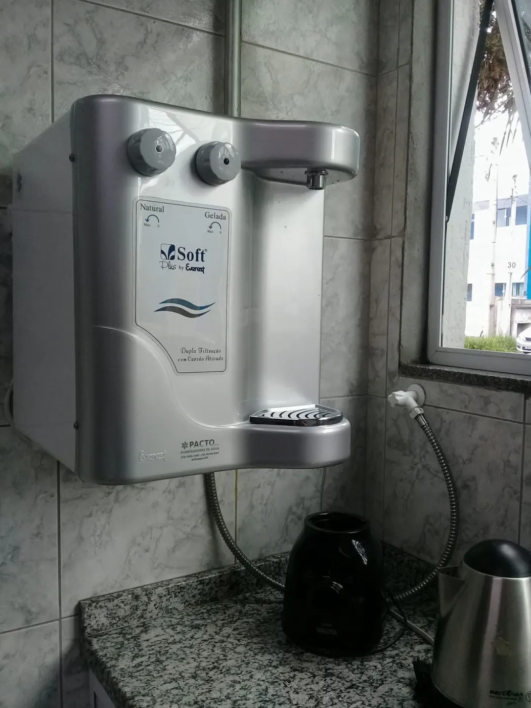 Purificador de água Soft Plus branco instalado em parede de cozinha ao lado de janela