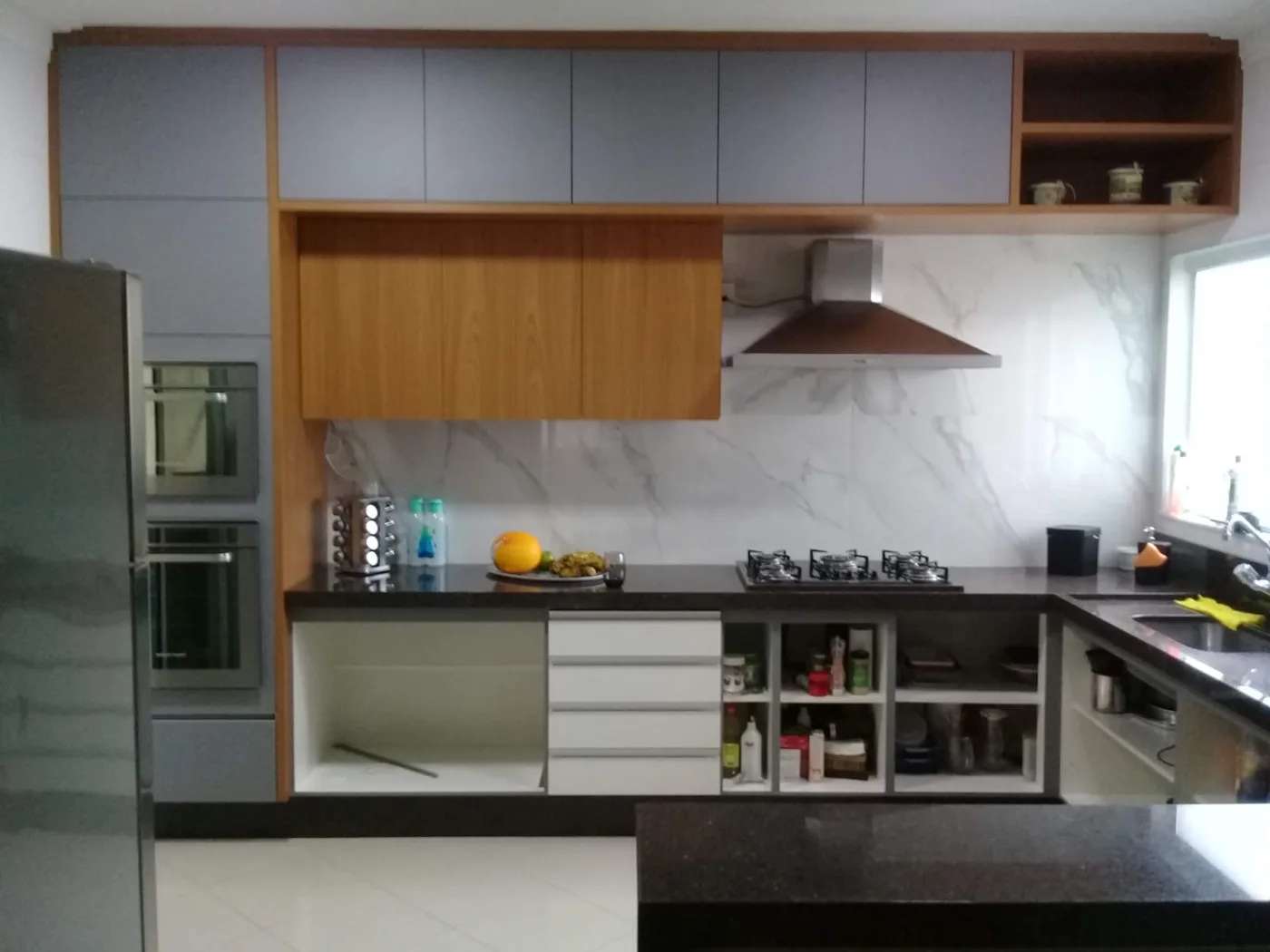Coifa instalada em cozinha planejada residencial com bancada de granito e revestimento de mármore