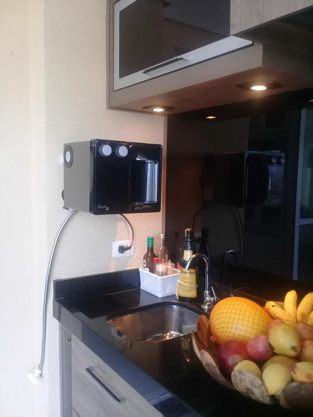 Purificador de água preto instalado na parede de uma cozinha gourmet com bancada preta