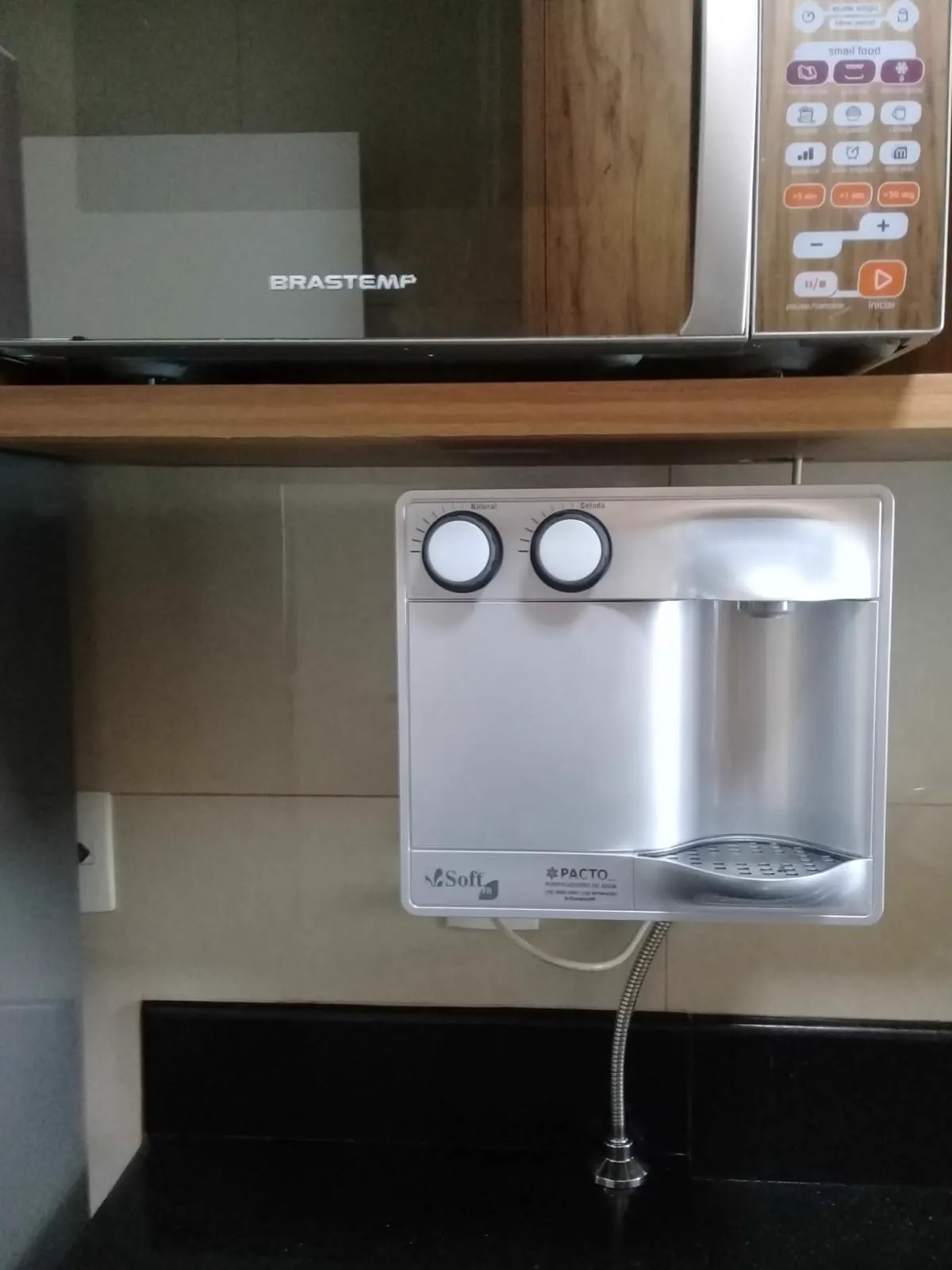 Purificador de água prata instalado na parede abaixo do micro-ondas
