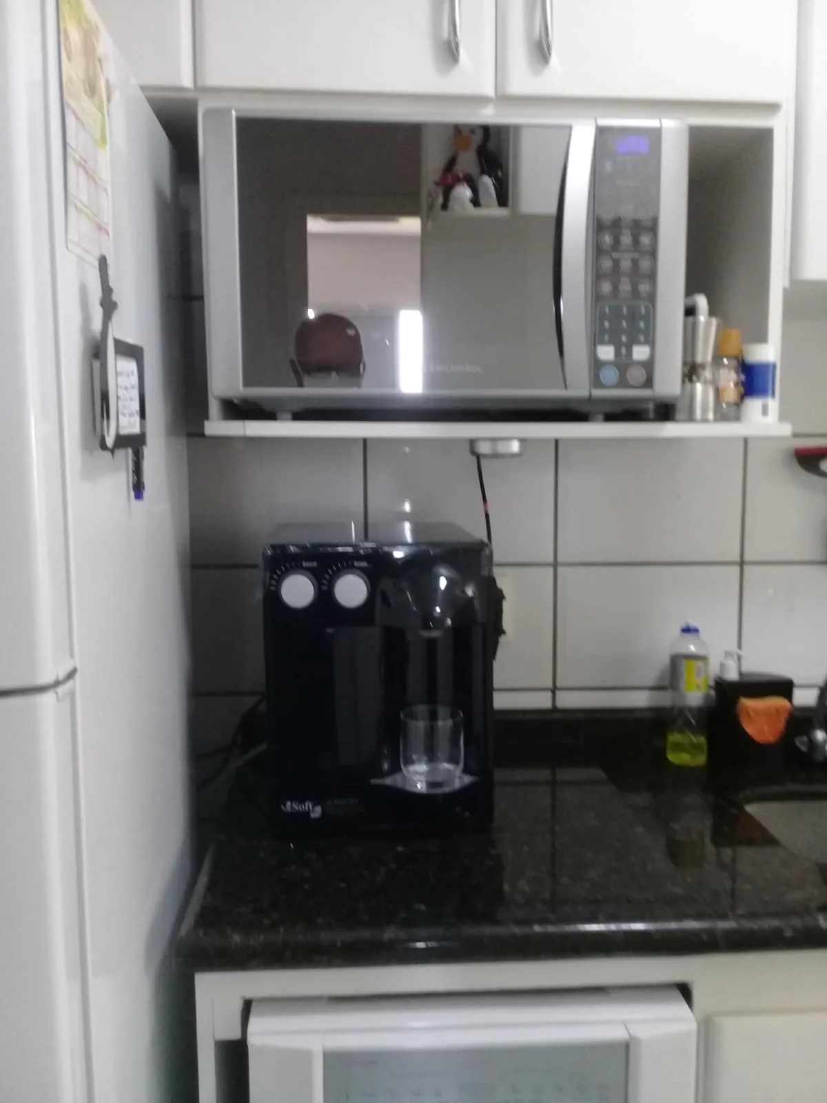 Purificador de água preto sobre bancada de granito escuro abaixo do nicho do micro-ondas