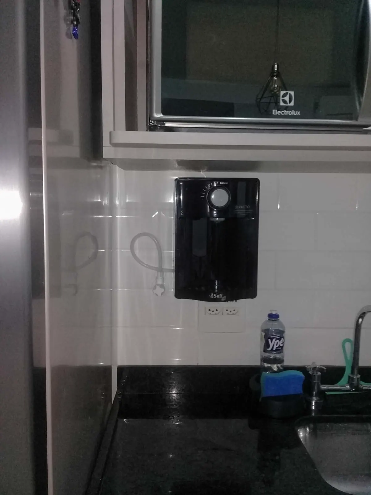 Purificador de água preto instalado na parede branca ao lado da geladeira