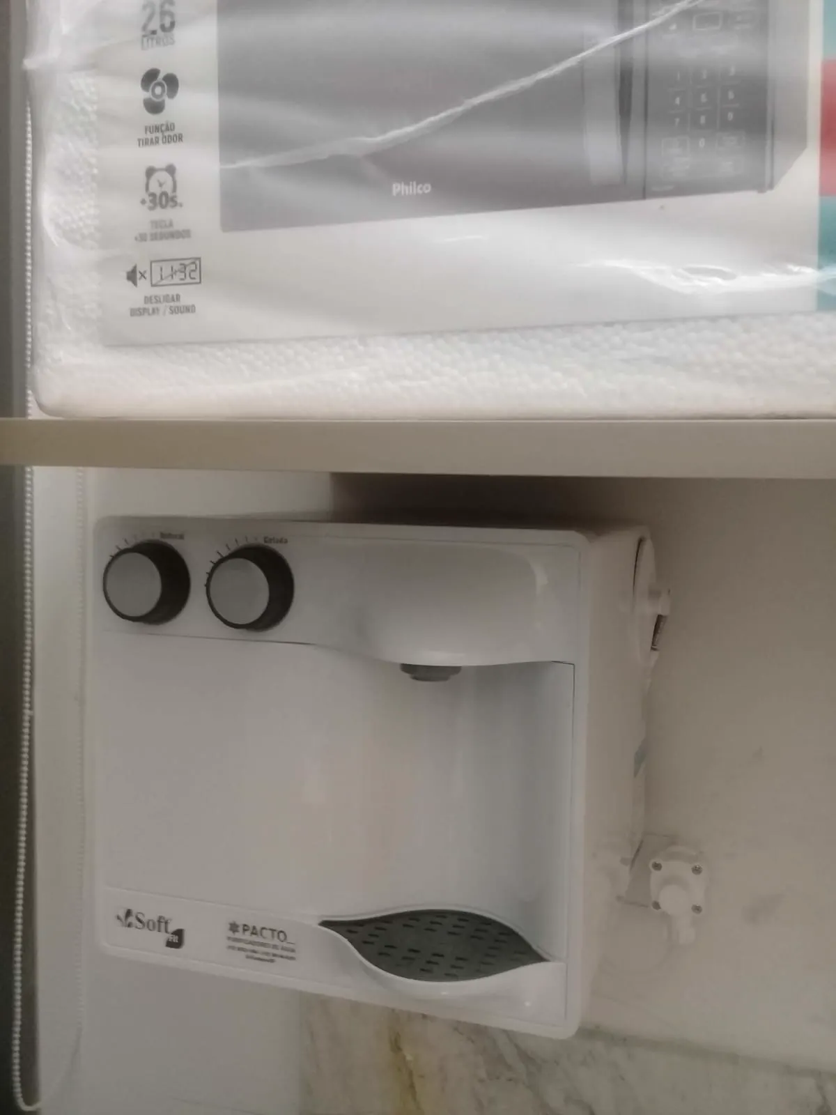 Purificador de água branco instalado na parede abaixo de uma prateleira de cozinha