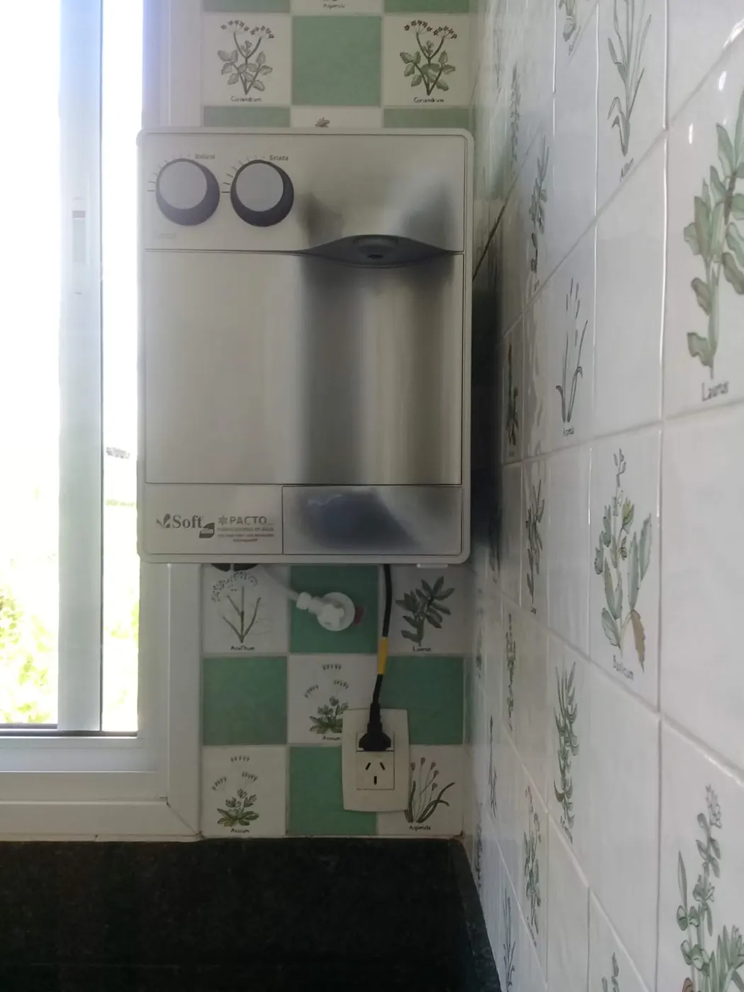 Purificador de água Soft branco instalado em parede de azulejos decorados ao lado de janela